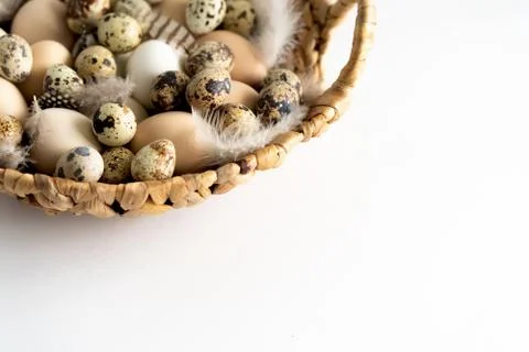 White and brown Easter eggs and feathers in a basket on white background. Stock Photos