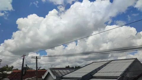 White and gray clouds with blue sky above the roofs of the village houses Stock Footage 274153256