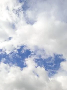 White and gray clouds drift across a blue sky, softly lit by sunlight. Stock Photos