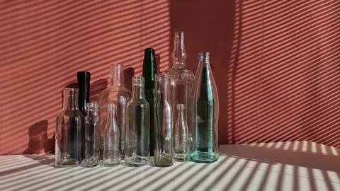 White and green glass empty bottles are on a table, illuminated by the sun Stock Footage 303929260