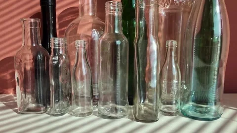 White and green glass empty bottles are on a table, illuminated by the sun Stock Footage 303929304