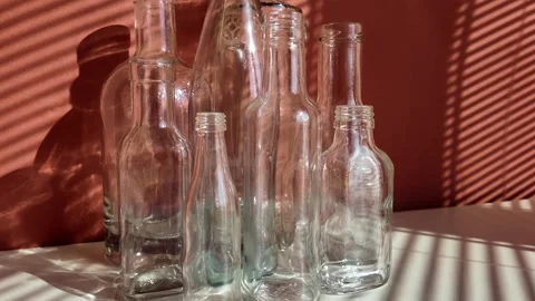 White and green glass empty bottles are on a table, illuminated by the sun Stock Footage 303929307
