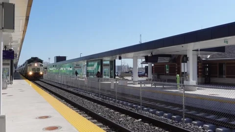 A white and green train coming to an outdoor train station platform Stock Footage 273533009