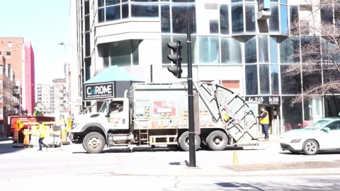 A white and grey rear-loader garbage truck operating on a sunny urban street in Stock Footage 334010184