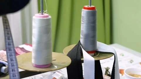 White and grey spools of thread unwinding from an industrial sewing machine 스톡 동영상 339754680