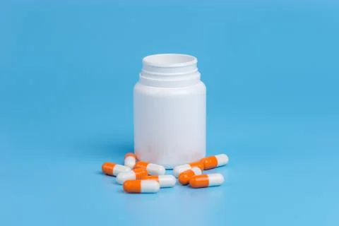 White and orange pills, tablets and white bottle on blue background. Stock Photos
