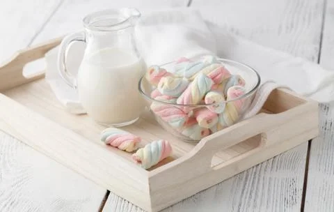 White and pink twisted marshmallows and a jug of milk on a white wooden table Foto stock