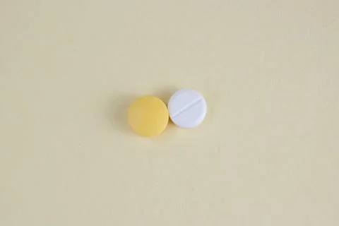 White and Yellow Medicine Tablets Isolated on Light Yellow Background with .. Stock Photos