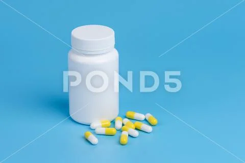 White and yellow pills, tablets and white bottle on blue background Stock Photos
