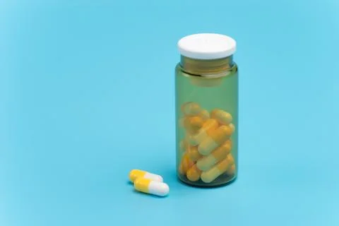 White and yellow pills, tablets and brown glass bottle on blue background Stock Photos