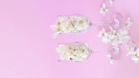 White apple blossoms falling into two crystal wine glasses Stock Footage 329609904