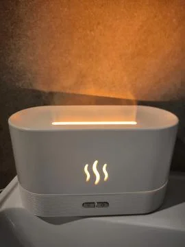 White aroma diffuser, air humidifier with flame effect, steam against warm Stock Photos