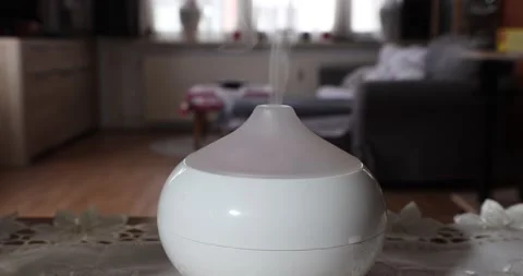 White aroma oil diffuser humidifier exhaling fragrance mist in a home interior Stock Footage 211172795
