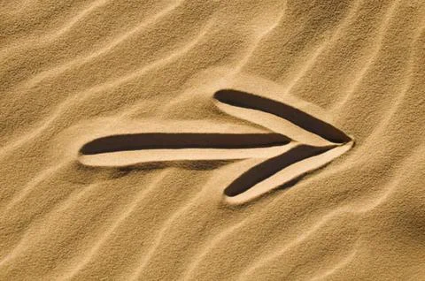 White arrow pointing on sandy beach Stock Photos