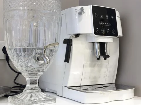 White automatic coffee machine standing next to a large crystal water dispe.. Stock Photos