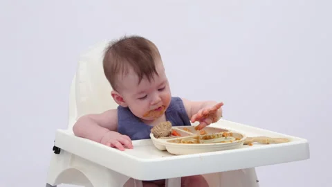 White background. An adorable baby eats independently from a plate 스톡 동영상 332263253