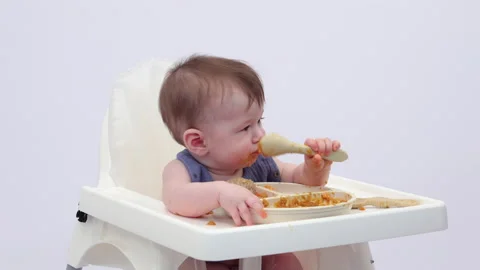 White background. An adorable baby eats independently from a plate Video stock 332263272
