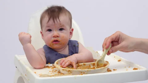 White background. An adorable baby eats independently from a plate Stock-Footage 332264800
