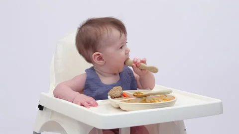 White background. An adorable baby eats independently from a plate Stock-Footage 332264896