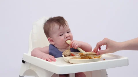 White background. An adorable baby eats independently from a plate Video stock 332265052