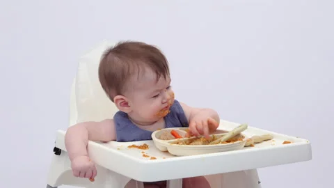 White background. An adorable baby eats independently from a plate Video stock 332267794
