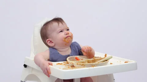 White background. An adorable baby eats independently from a plate Video stock 332269768