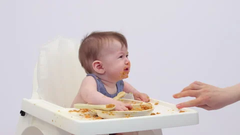 White background. An adorable baby eats independently from a plate Video stock 332270048