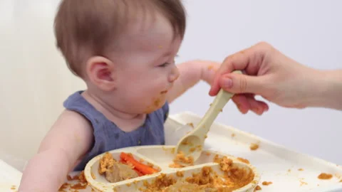 White background. An adorable baby eats independently from a plate Stock-Footage 332270820
