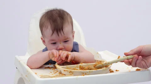 White background. An adorable baby eats independently from a plate Video stock 332270856