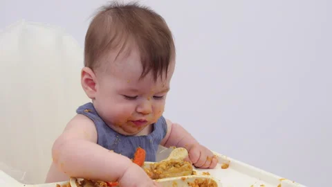 White background. An adorable baby eats independently from a plate Video stock 332270906
