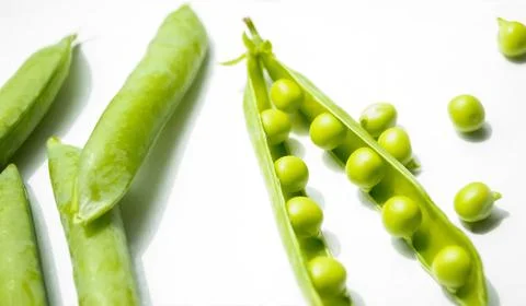 On a white background is an open pod of green peas, and next to it lie closed Stock Photos
