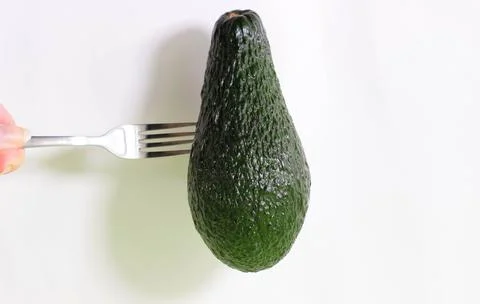 On a white background, part of an avocado with a fork stuck in it. The concep Fotos Stock