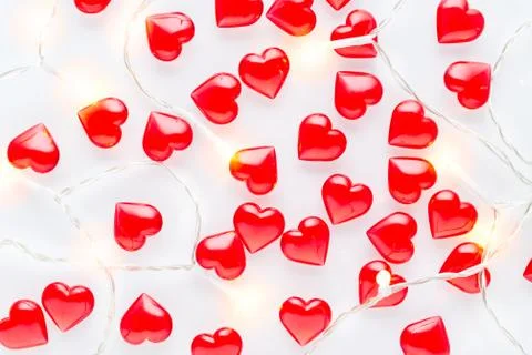 White background with red hearts pattern and garland lights, flat lay Stock Photos