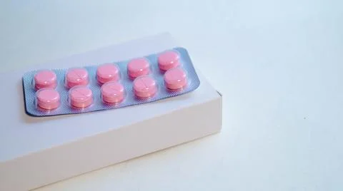 On a white background, a small box on which lies a blister with pink tablets Stock Photos