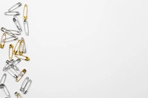 White background with small shiny silver and gold safety pins positioned Stock Photos