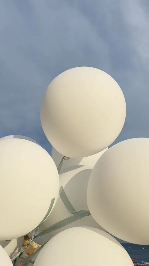 White balloons flutter in the wind against a serene sea a blue cloudy sky Stock Footage 283066827