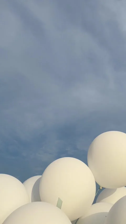 White balloons flutter in the wind against a blue cloudy sky Stock Footage 283066839