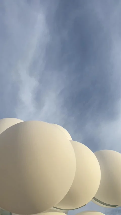 White balloons flutter in the wind against a blue cloudy sky Stock Footage 283066856