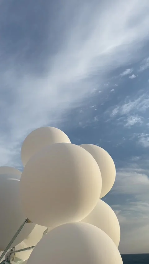 White balloons flutter in the wind against a blue cloudy sky Stock Footage 283066868