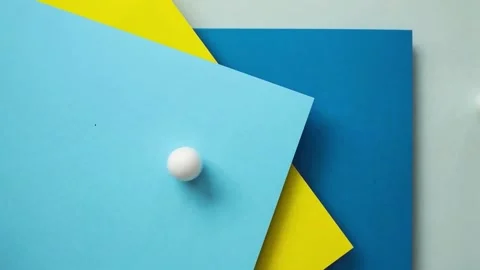 White balls rolling on colored paper backgrounds. Video stock 336814123