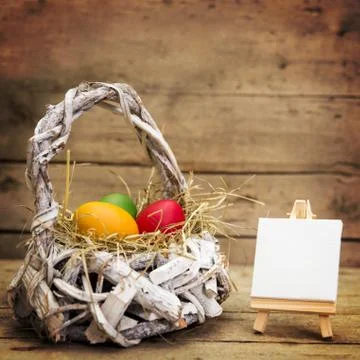 White basket with easter eggs, empty canvas with copyspace, wooden background Stock Photos