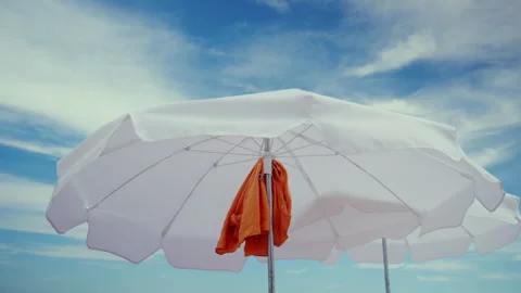 White beach umbrella creating shade against a blue sky with light clouds, Stock Footage 339781123