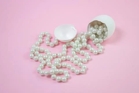 White beads scattered from the broken egg. Beads on a pink background.  Stock Photos