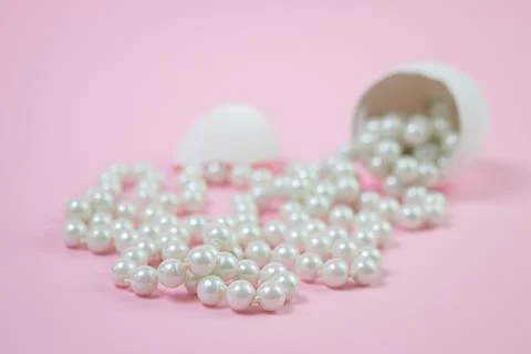 White beads scattered from the broken egg. Beads on a pink background.  Stock Photos