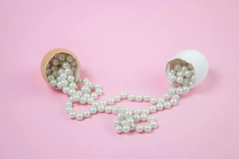 White beads scattered from the broken egg. Beads on a pink background.  Stock Photos