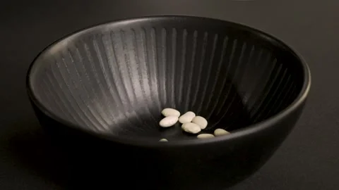 White beans falling into black bowl on black background 4k 10bit 120fps Stockbeeldmateriaal 332620336