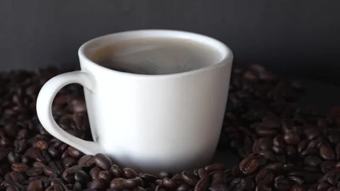 A white beautiful cup of coffee on a table with coffee grounds on turn table, on Stock-Footage 243295743