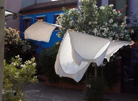 White bed sheets spread to dry in the sun in a city in the mediterranean area Stock Photos