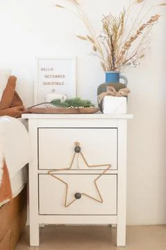 White bedside table, with Christmas decorations and dried flowers in a blue vase Stock Photos