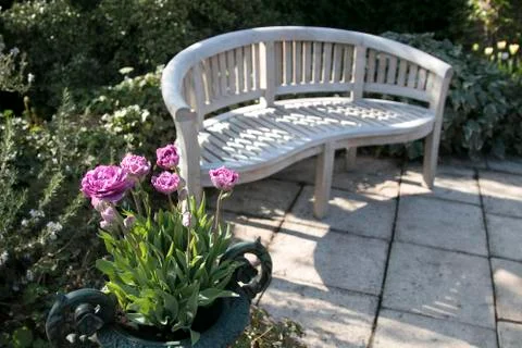 White bench in the garden next to pink tulips Stock Photos
